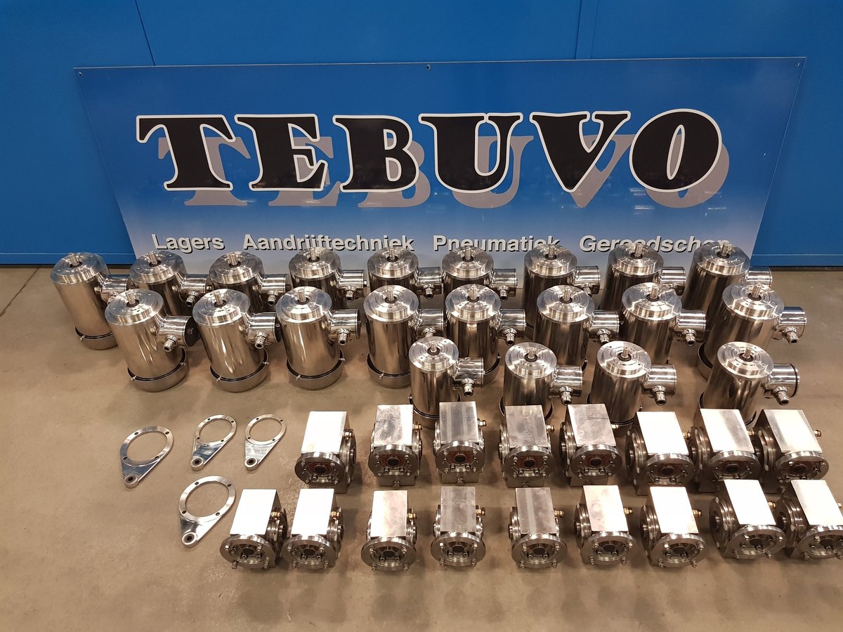 Display of industrial components with TEBUVO branding, including metallic cylinders and rectangular parts arranged on a tan surface with blue backdrop