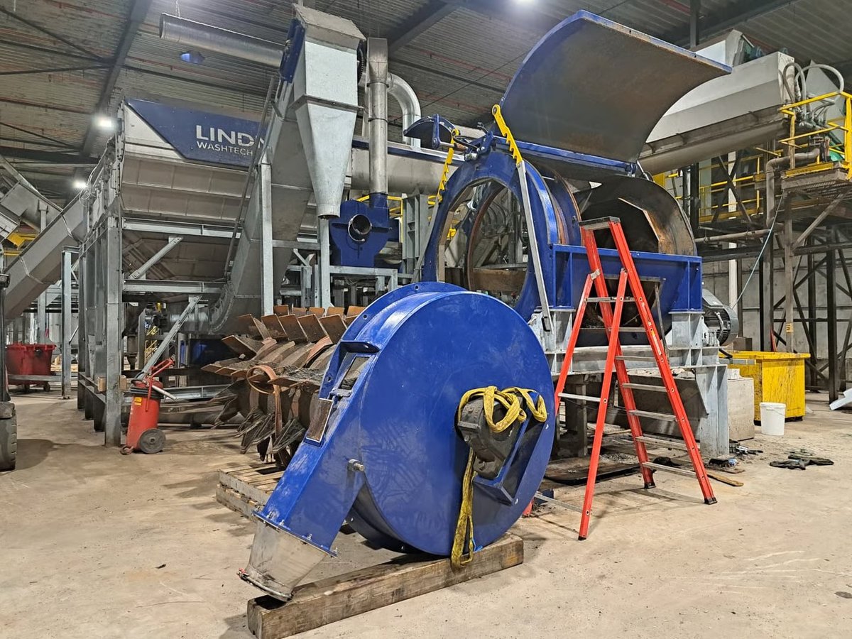 Blue concrete mixer truck under maintenance in an industrial warehouse with red ladder and equipment visible