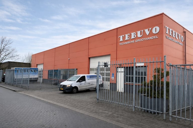 Orange brick TEBUVO commercial building with white delivery van parked outside behind metal gate fence